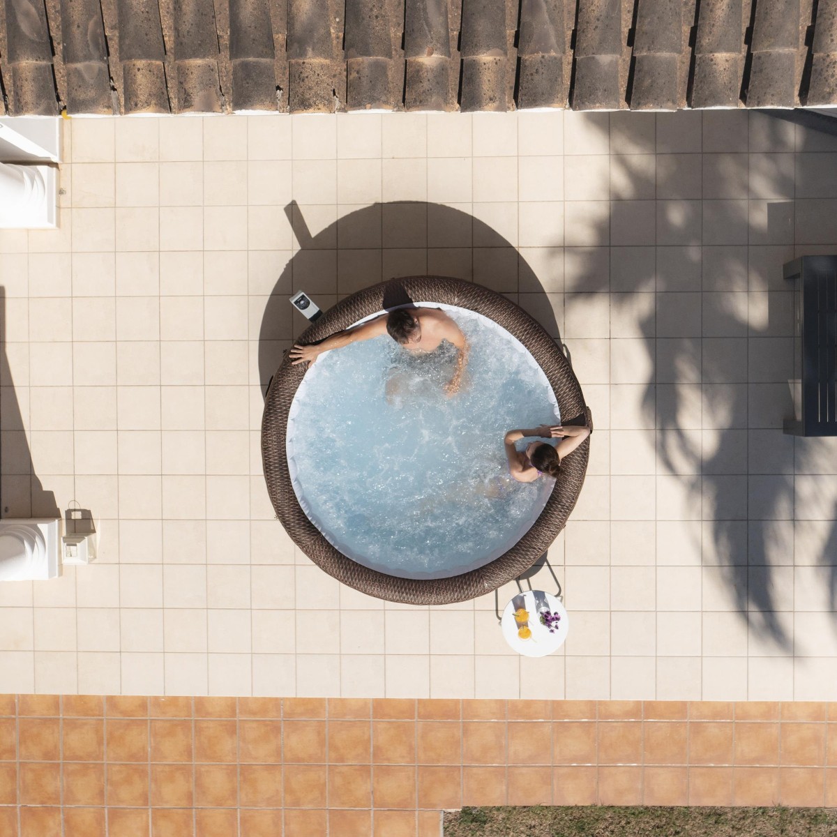 Widok z góry na okrągłe jacuzzi Lay-Z-Spa Bali z bąbelkami, umieszczone na jasnym tarasie. Widoczna struktura rattanu PVC w brązowym odcieniu oraz panel sterowania.